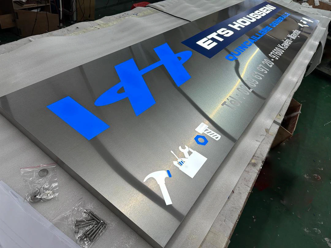 Enseigne tôle ajourée inox - ETS Housseni Enseigne en tôle ajourée inox brossé avec lettrage bleu et blanc réalisée pour ETS Housseni quincaillerie générale